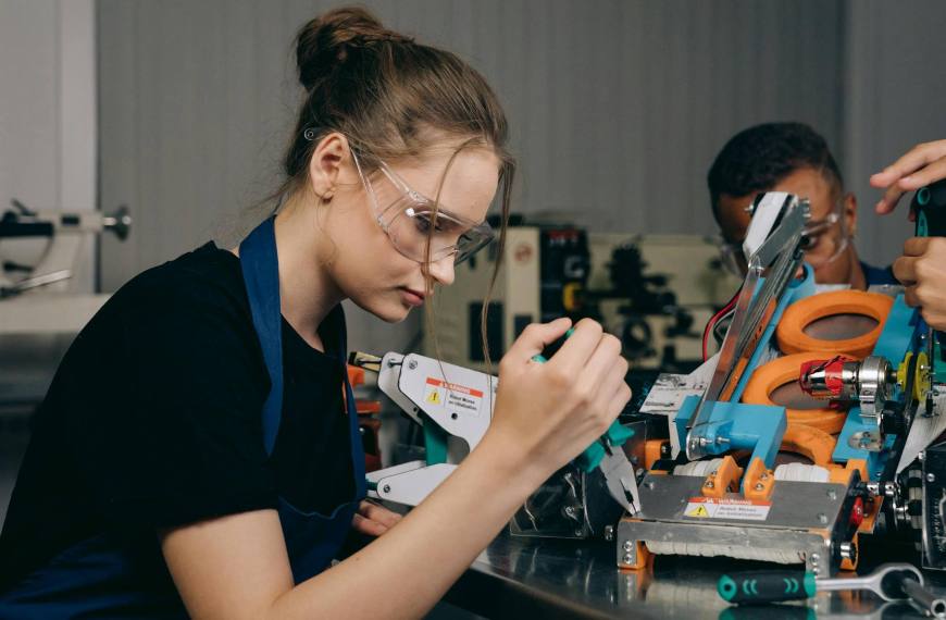 Female engineer in a workshop assembling robots with precision tools and safety gear.