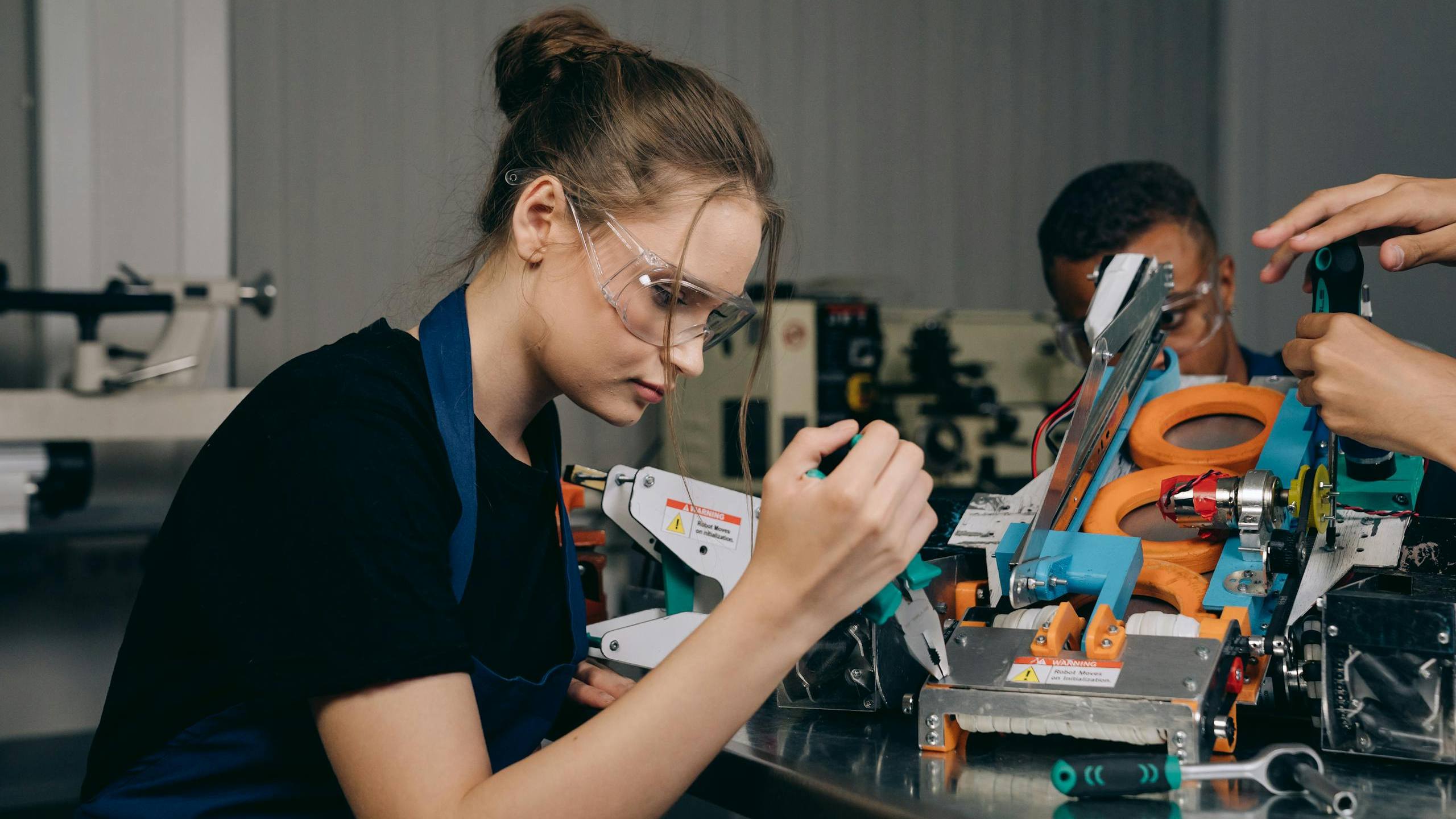 Female engineer in a workshop assembling robots with precision tools and safety gear.